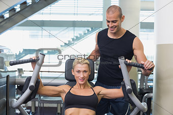 Trainer assisting woman on fitness machine at gym