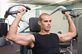 Serious young man working on fitness machine at gym