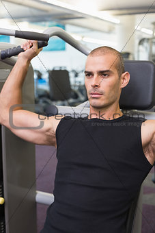 Serious young man working on fitness machine at gym