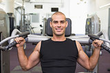 Smiling young man working on fitness machine at gym