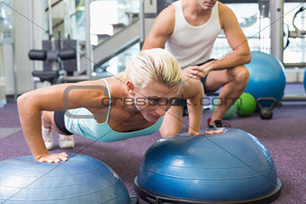 Male trainer assisting woman with push ups at gym