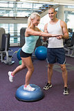 Trainer assisting woman with stretching exercises at gym