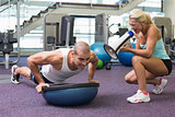 Trainer assisting man with push ups at gym
