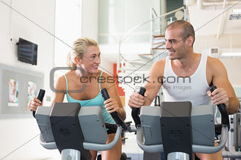 Fit couple working on exercise bikes at gym