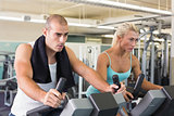 Fit couple working on exercise bikes at gym