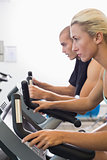 Determined fit couple working on exercise bikes at gym