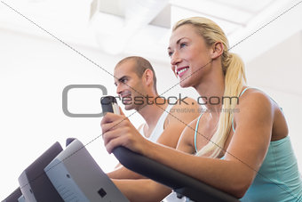 Fit young couple working on exercise bikes at gym