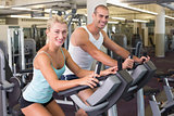 Fit young couple working on exercise bikes at gym