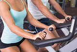 Mid section of couple working on exercise bikes at gym