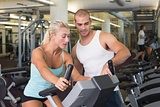 Trainer assisting woman with exercise bike at gym