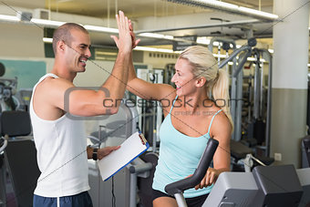 Trainer giving high five to his client on exercise bike at gym