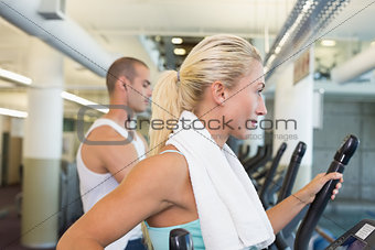 Side view of couple working on x-trainers at gym