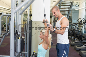 Trainer assisting young woman on a lat machine in gym