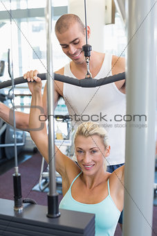 Male trainer assisting woman on lat machine in gym
