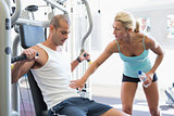 Trainer assisting man on fitness machine at gym