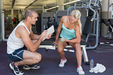 Male trainer assisting woman with dumbbell in gym