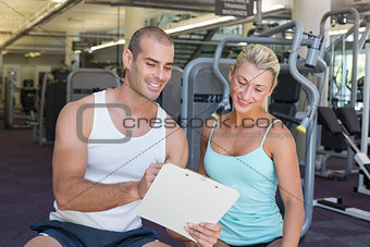Woman discussing her performance on clipboard with a trainer at gym