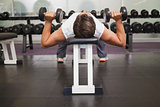 Fit man lifting dumbbells lying on the bench