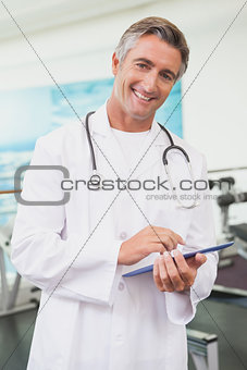 Confident doctor standing in fitness studio using tablet pc