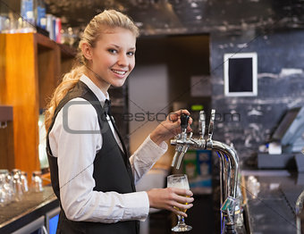 Barmaid pulling a glass of beer while looking at camera