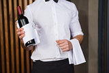 Handsome waiter holding a bottle of red wine and a towel