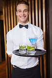 Cheerful young waiter holding tray with cocktails