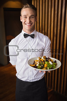 Smiling waiter showing plate of salad to camera