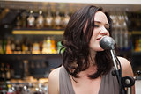 Brunette haired woman singing in a microphone