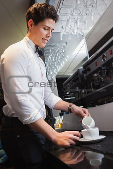 Barista pouring milk into cup of coffee