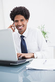 Happy businessman phoning and using laptop