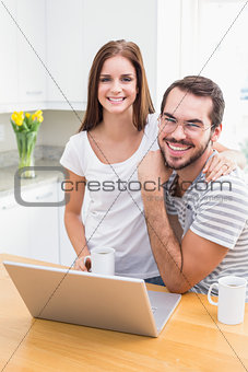 Young couple smiling at the camera using laptop