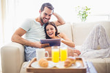 Cute couple relaxing on couch with tablet at breakfast