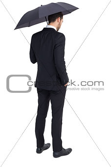 Thoughtful businessman under umbrella with hand in pocket