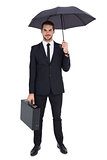 Smiling businessman under umbrella while holding briefcase