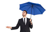 Cheerful businessman holding umbrella with hand out