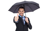 Positive businessman under umbrella with thumbs up