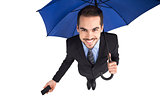 Smiling businessman under umbrella holding smartphone