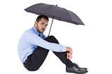 Unsmiling businessman holding umbrella sitting on the floor