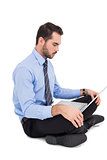 Cheerful businessman sitting on the floor using laptop