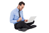 Cheering businessman sitting using his laptop