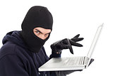 Hacker in balaclava standing and typing on laptop