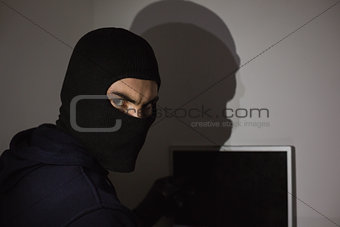 Hacker in balaclava hacking laptop while looking at camera