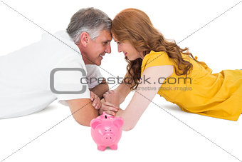 Casual couple lying on floor with piggy bank