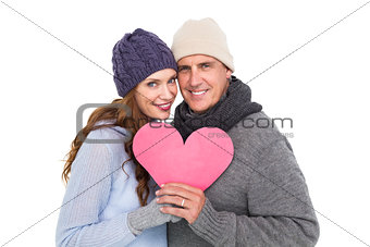 Happy couple in warm clothing holding heart