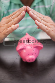 Mans hands sheltering  piggy bank