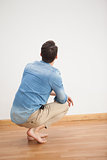 Casual man crouching on floor looking at wall
