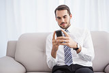 Businessman sending a text on the couch