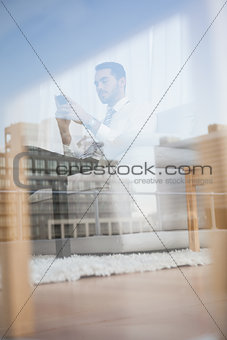 Businessman texting on his couch seen through glass