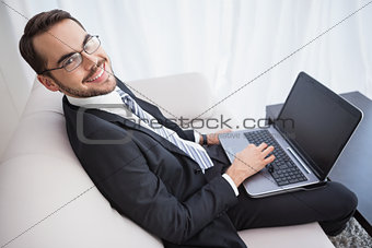 Smiling businessman using laptop on his couch