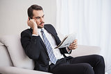 Businessman making a call on his couch reading newspaper